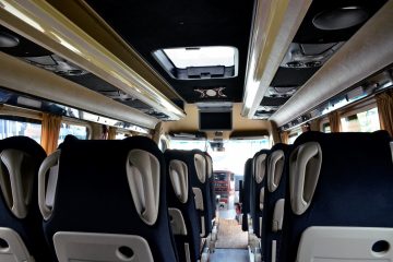 Interior microbuz cu scaune negre, ecran suspendat și bord
